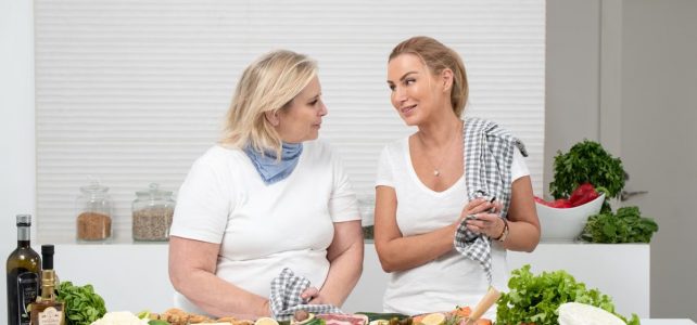 Zbilansowana dieta dla całej rodziny Two women in a kitchen preparing fresh vegetables and cheese with olive oil and spices.