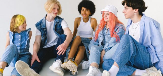 Korzyści płynące z regularnej aktywności fizycznej Group of cheerful diverse teenager friends talking to each other while sitting together on floor against white background